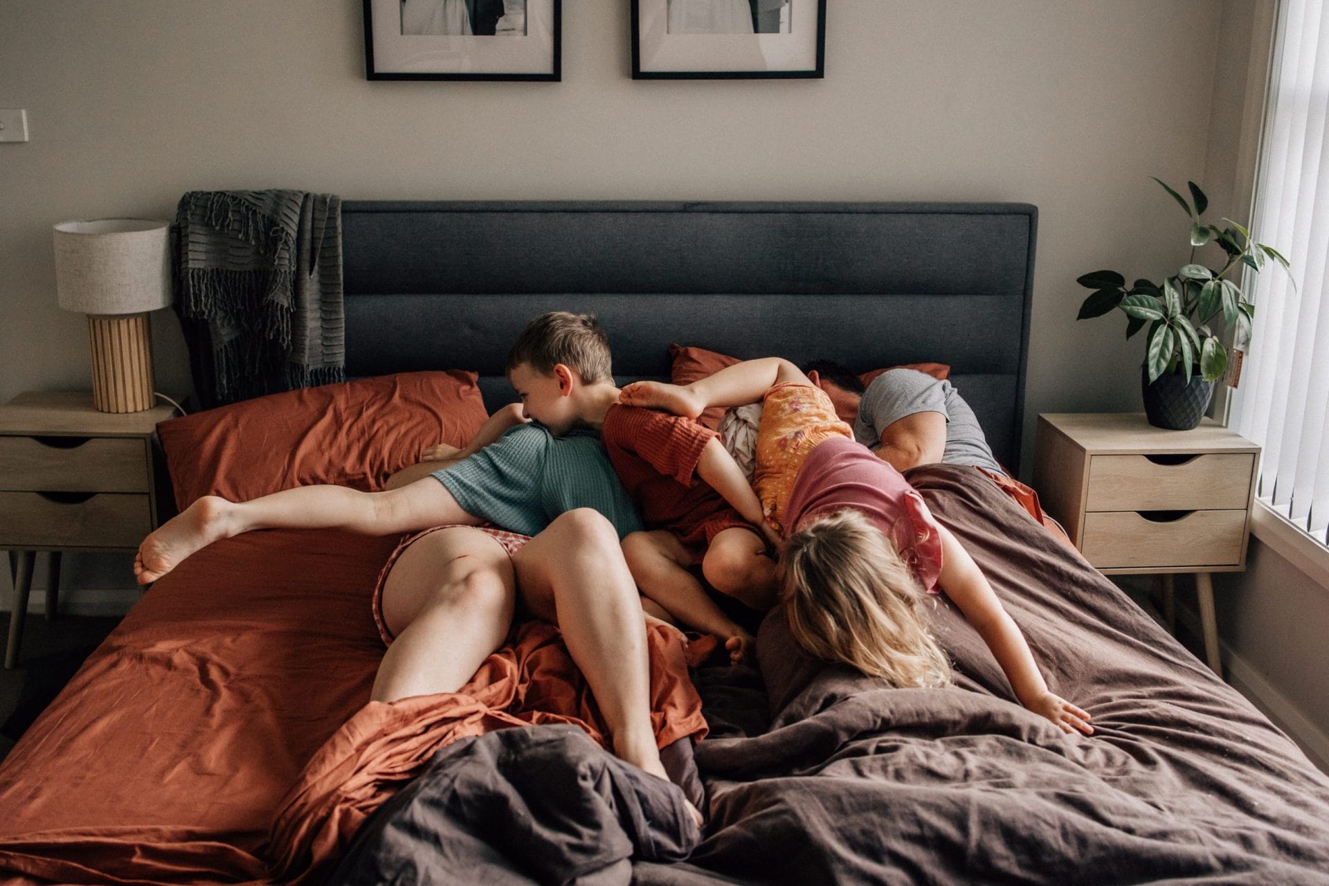 The need for perfection is stealing our joy 2 Three children lie playfully on a bed with scattered pillows in a warmly decorated bedroom.