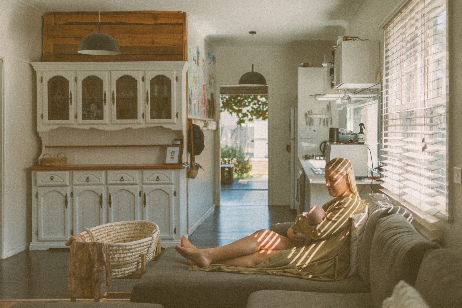 A person in a striped robe sits relaxed on a couch, reading a book in a cozy sunlit living room with vintage furniture.