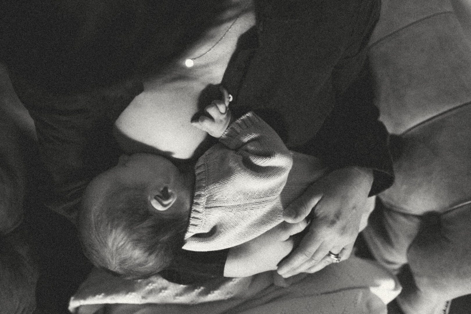 A monochrome photo of a mother cradling her sleeping infant close to her chest.