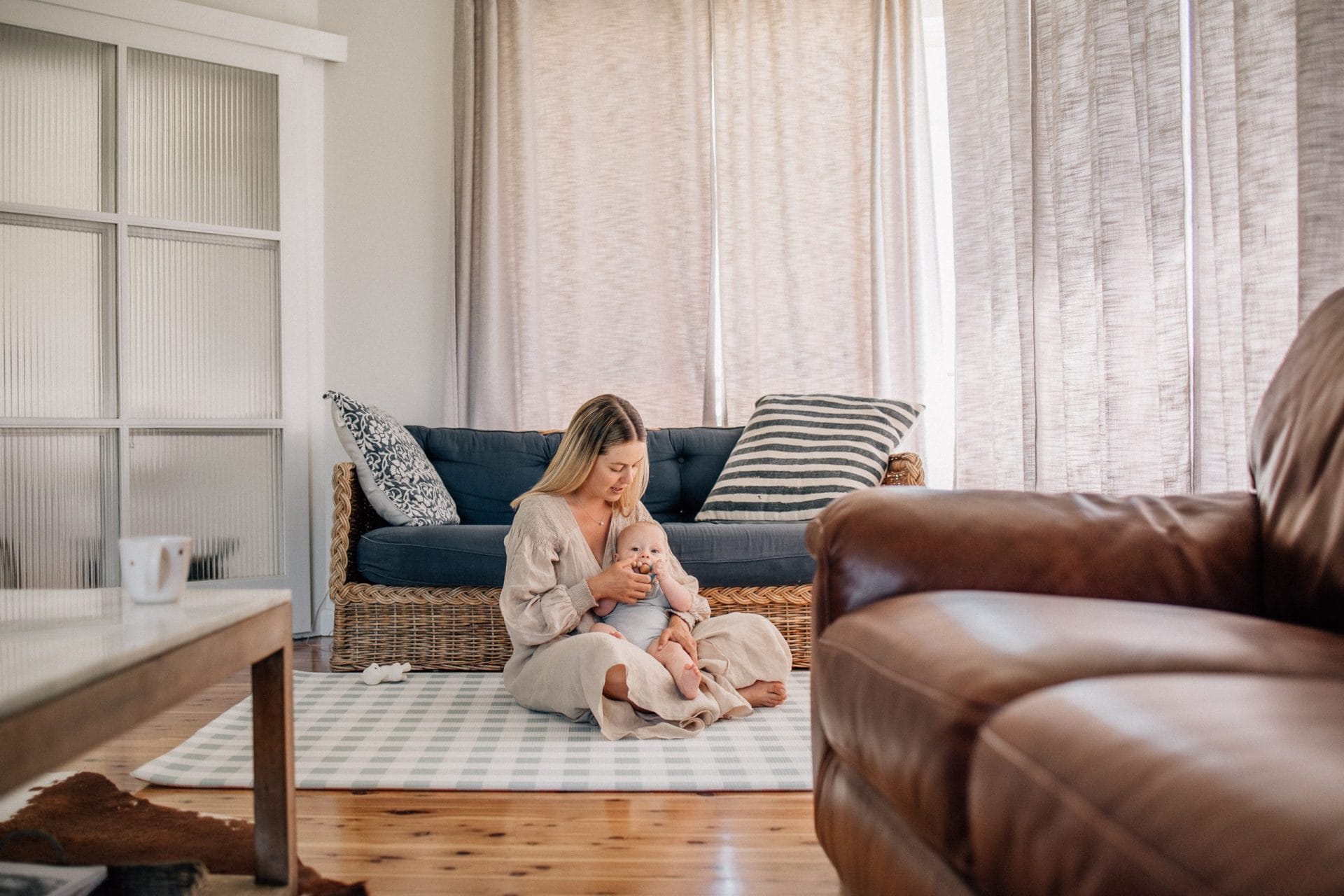 A woman sitting on a couch, lovingly holding and looking at a baby in a cozy, well-lit living room.