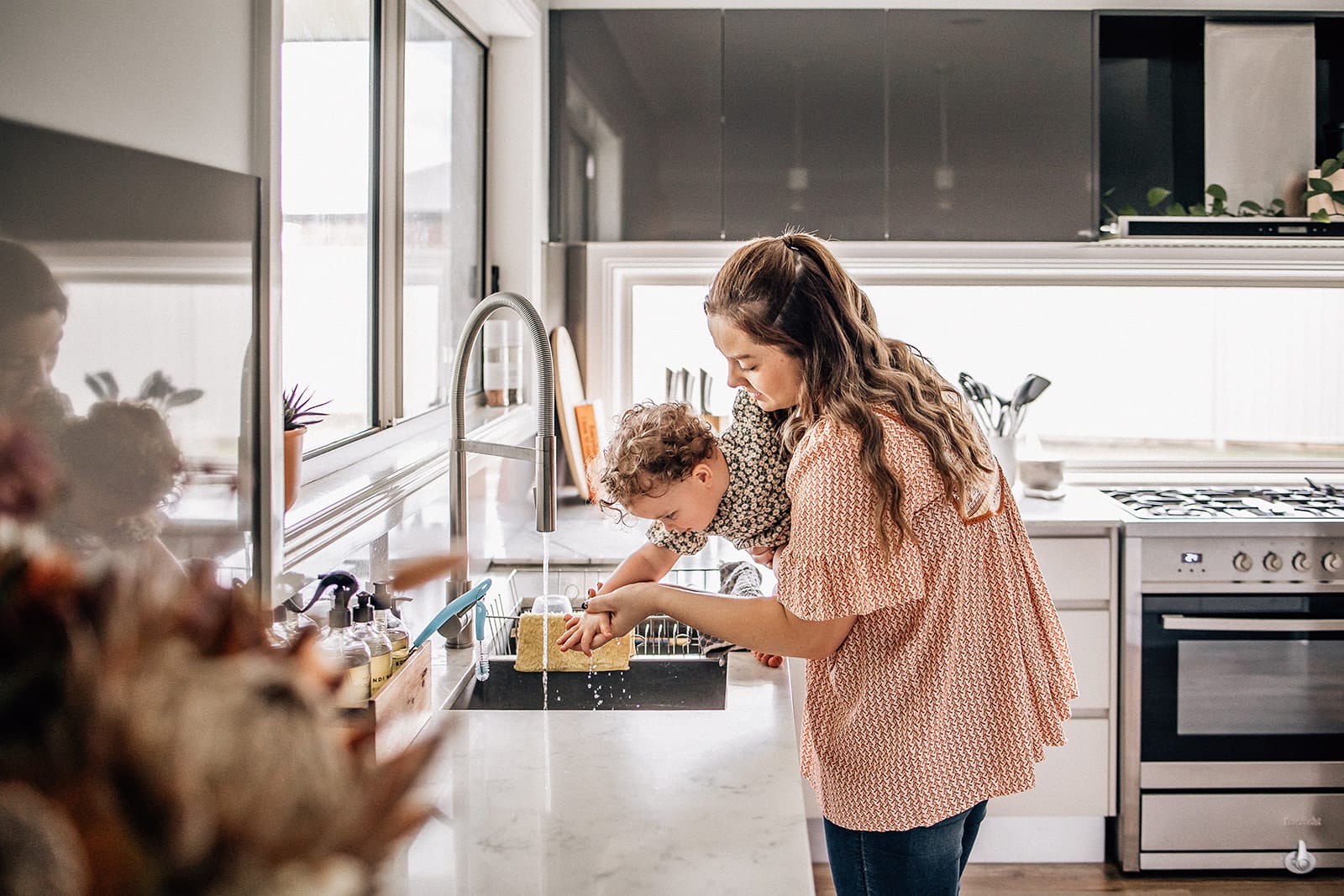 Mother's Day. One day of the year isn't enough. 1 A young girl and a boy washing dishes together in a modern kitchen.