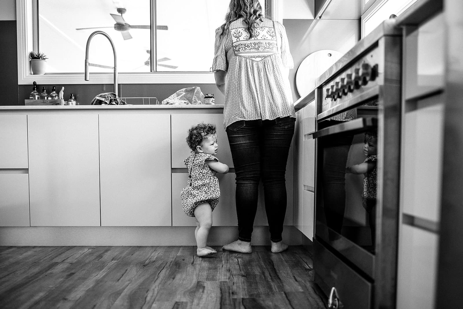 A toddler standing next to a woman by an open oven in a modern kitchen, both looking inside.