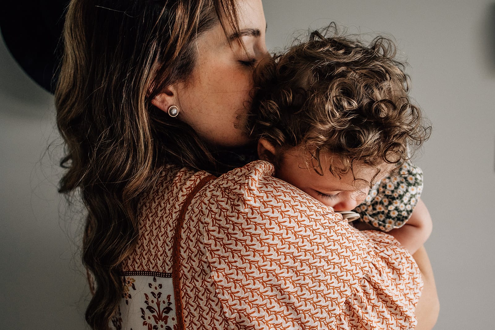 Mother's Day. One day of the year isn't enough. 2 A woman gently kisses the head of a curly-haired child she is holding in a warm embrace.