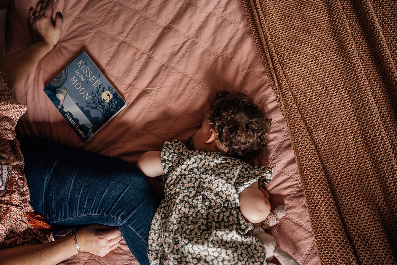 Mother's Day. One day of the year isn't enough. 5 A child lying face down on a bed next to a woman, with a book titled "kiss good night" visible.