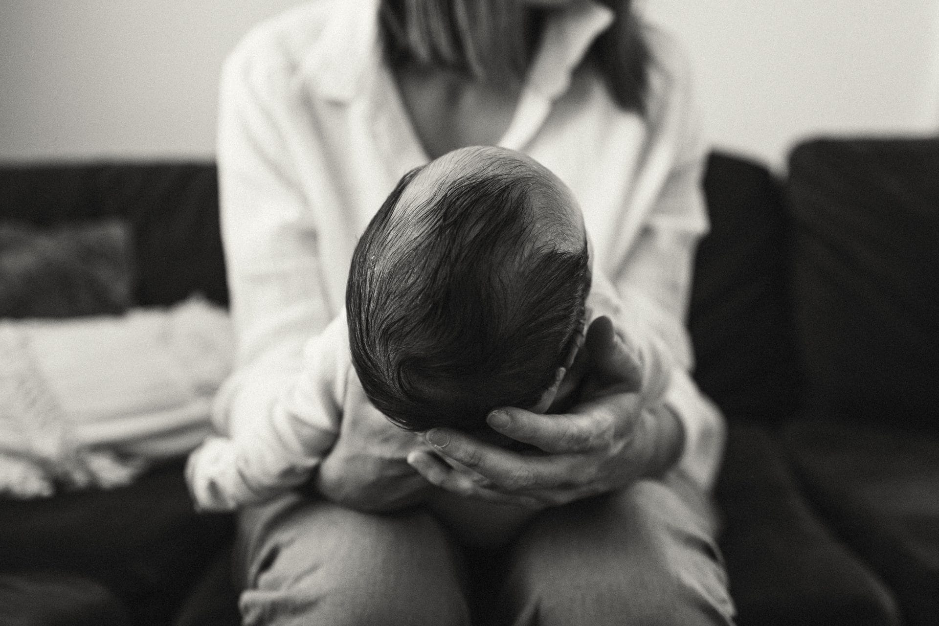 A woman sitting on a couch, cradling her head in her hands, showing signs of distress or sadness, in black and white.